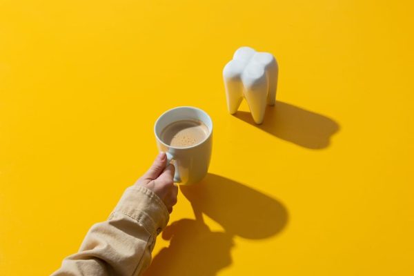 female hand holds cup of coffee next to tooth on y 2022 05 01 23 35 44 utc